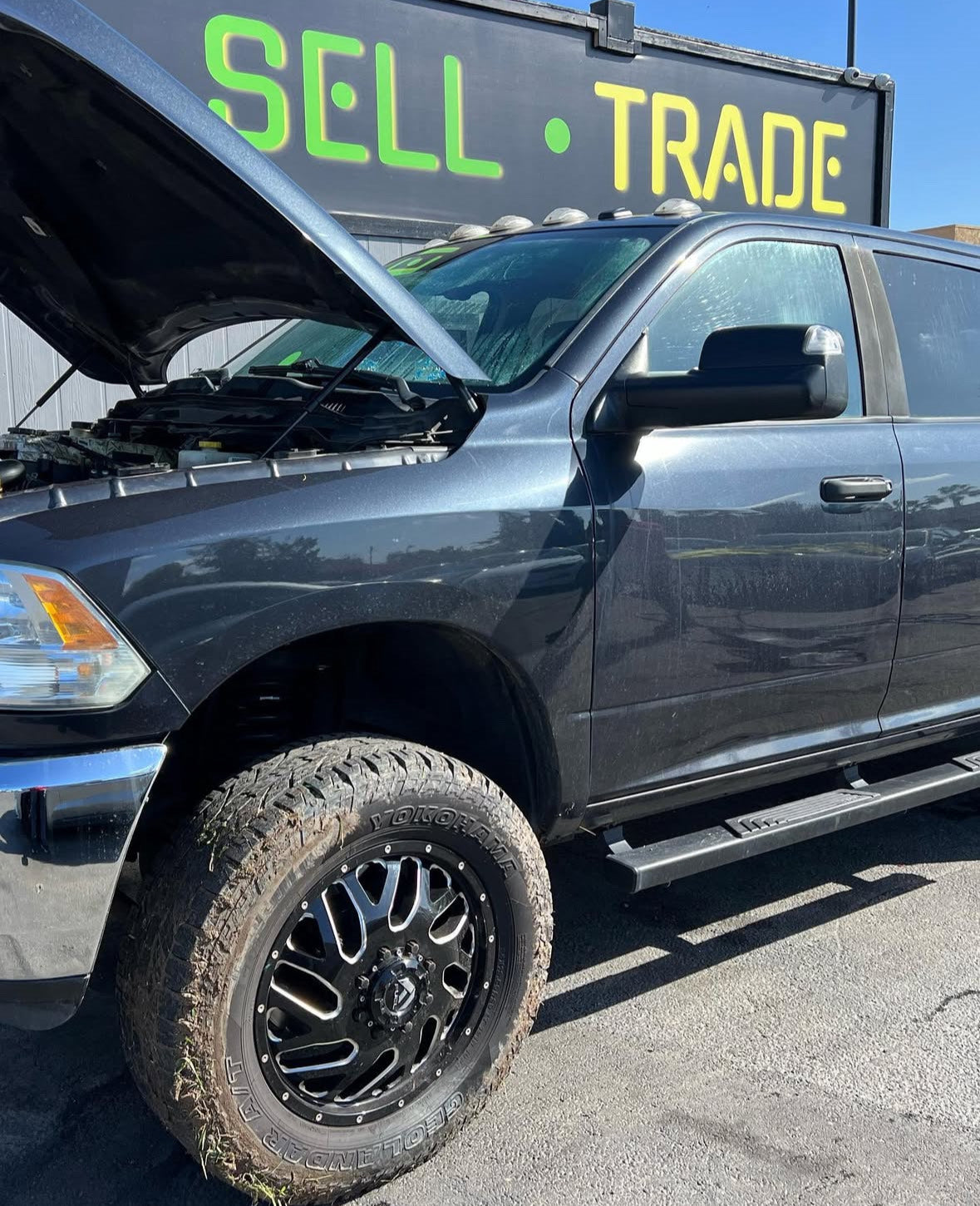 Black pickup truck with open hood in a lot.
