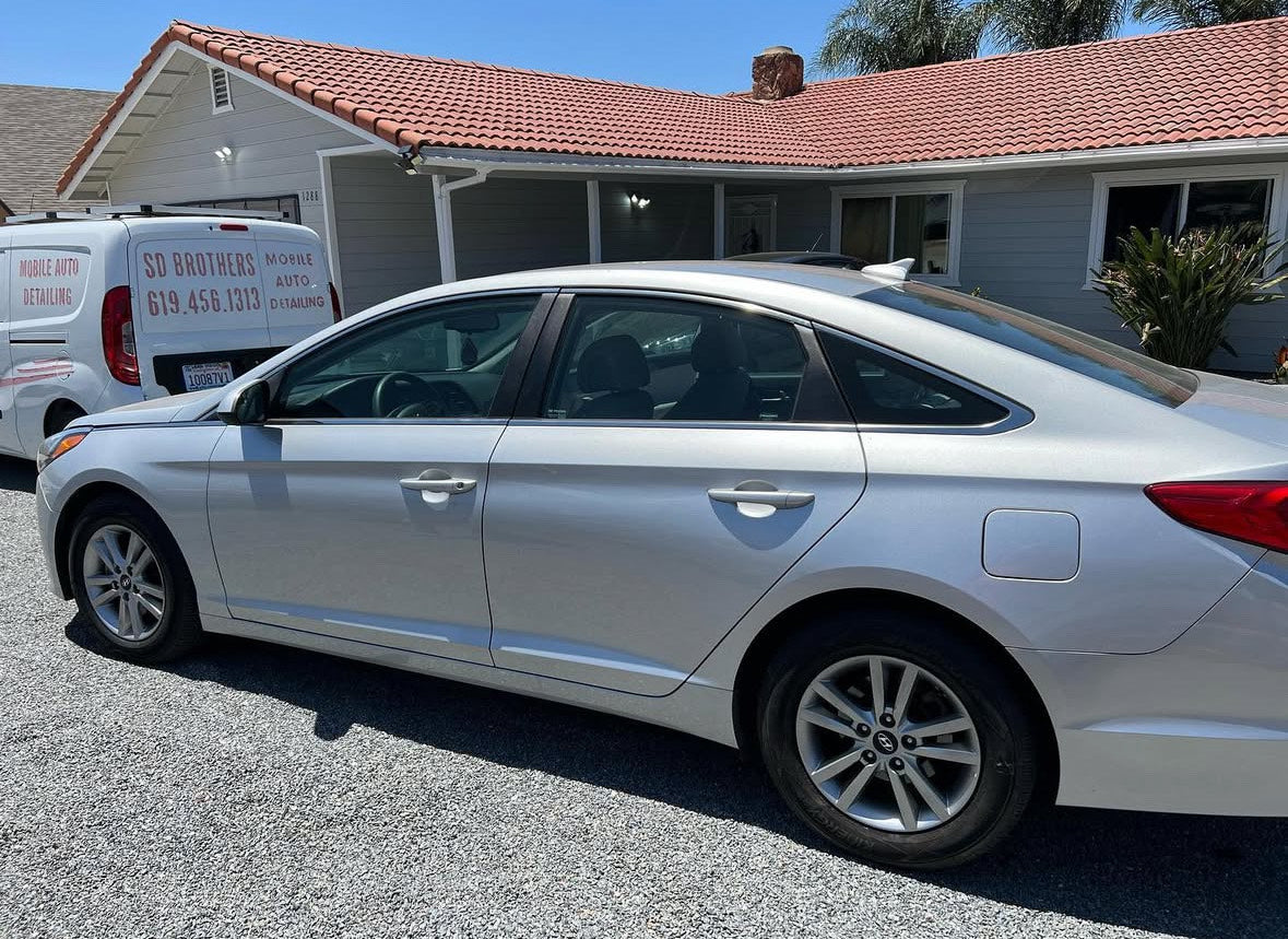 White car parked in front of a house with a clear sky.